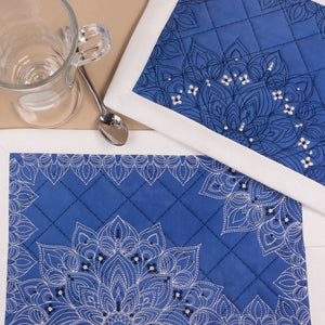 Blue placemats with white embroidery and bead details on a table setting.