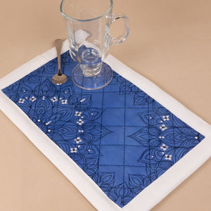 Blue placemat with white border on a beige surface, featuring a glass and spoon.