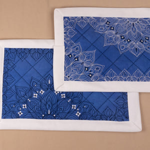 Two blue placemats with white embroidery on a beige background