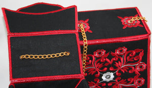Black jewelry box with red floral embroidery and a gold chain on a white background