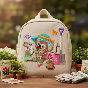 Beige backpack with embroidered design of a bear and mouse in a garden setting, surrounded by plants and gardening items.