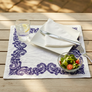 Dining setup with a glass of water, plate, knife, fork, and small bowl of salad on a decorative placemat.