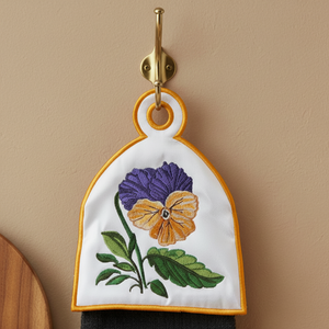 Embroidered floral towel hanging on a wall hook against a beige background