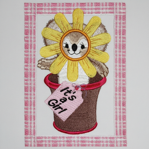 Embroidered design of a hedgehog with a flower head and 'It's a Girl' sign on a pink and white checkered background.