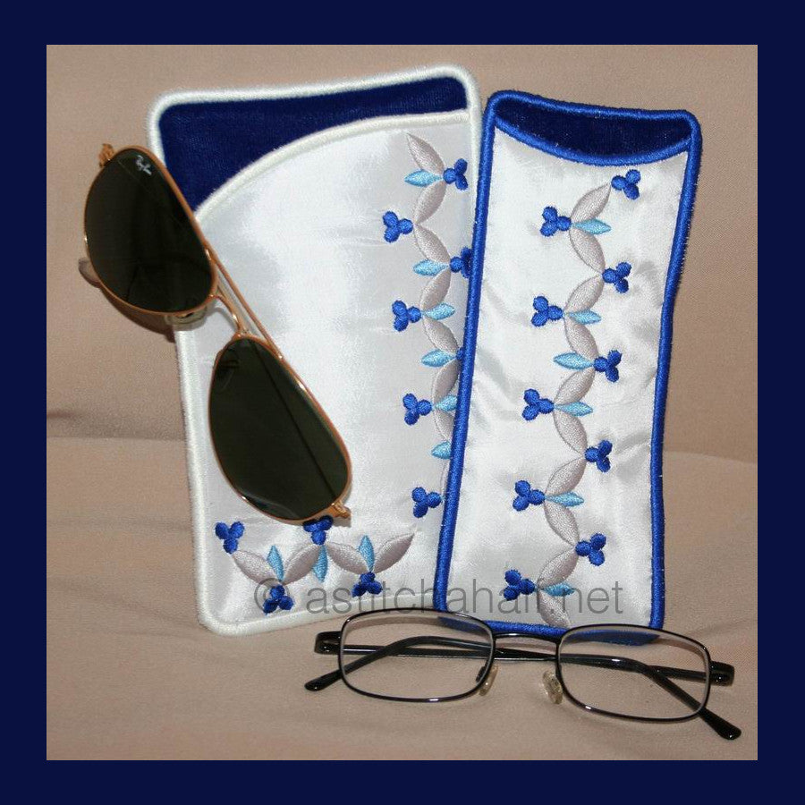 Royal Eyeglass Cases 02 - a-stitch-a-half. Two embroidered eyeglass cases with blue binding featuring delicate vine patterns with small blue flowers and gray leaves on white fabric. 