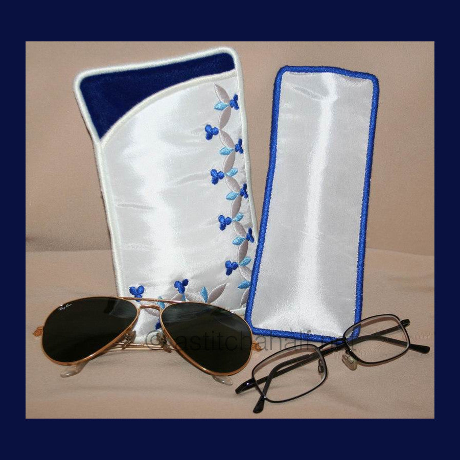 Royal Eyeglass Cases 02 - a-stitch-a-half. Two embroidered eyeglass cases with blue binding featuring delicate vine patterns with small blue flowers and gray leaves on white fabric. 