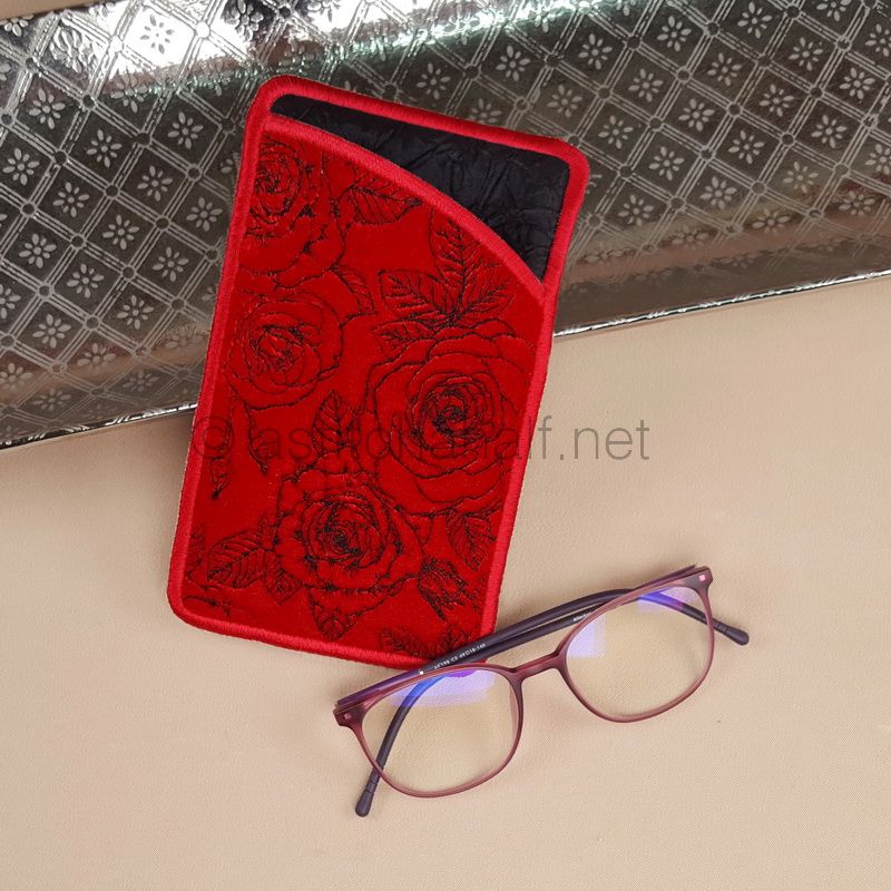 A red eyeglass case with a floral pattern displayed next to a pair of glasses, placed on a textured silver surface.