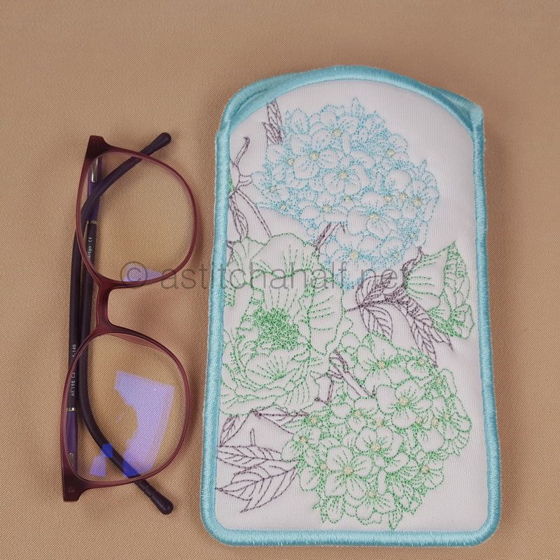A reading pillow with a hydrangea pattern and eyeglasses placed on top of it, set against a beige background.