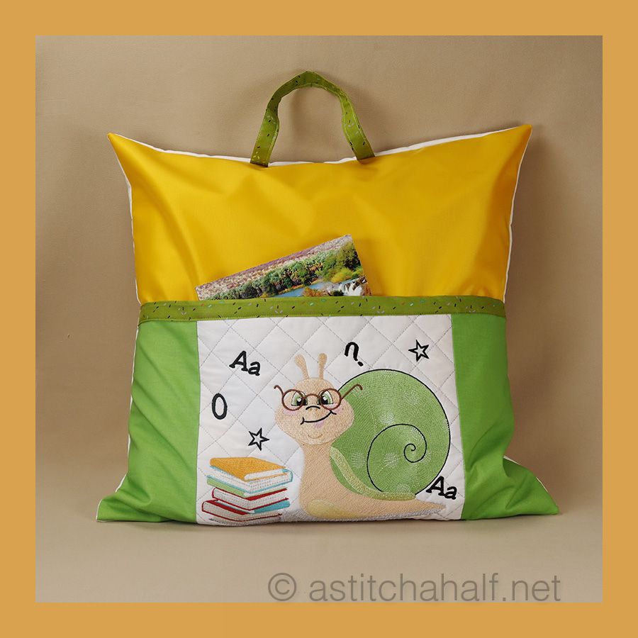 A reading pillow featuring an embroidered design of a snail with glasses, carrying a stack of colorful books, set against a quilted background with letters and stars.