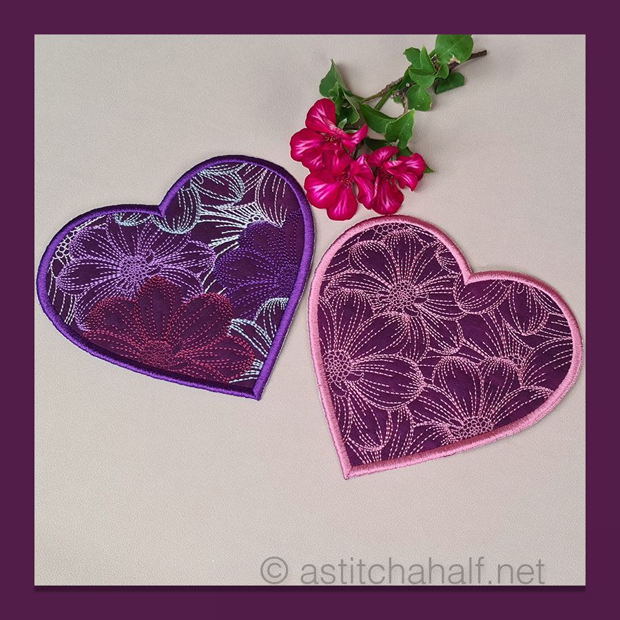 Heart-shaped embroidered coasters with a white cup and flowers on a wooden surface