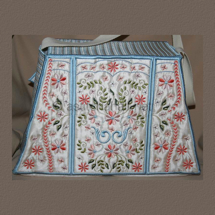 A person holding a multicolored floral tote bag with a white strap and blue trim.