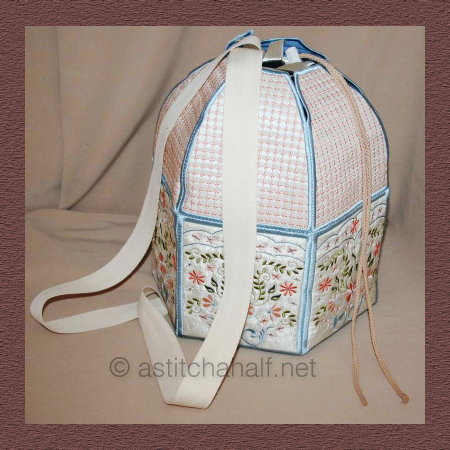 Signature Back Pack - a-stitch-a-half. A handmade drawstring bag or project bag with embroidered panels featuring geometric cross-stitch patterns in coral/pink and floral motifs with small flowers and leaves. It has blue trim, white fabric handles, and drawstring closures.