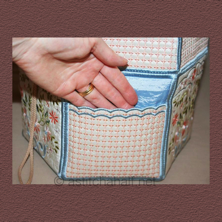 Signature Back Pack - a-stitch-a-half. A handmade drawstring bag or project bag with embroidered panels featuring geometric cross-stitch patterns in coral/pink and floral motifs with small flowers and leaves. It has blue trim, white fabric handles, and drawstring closures.